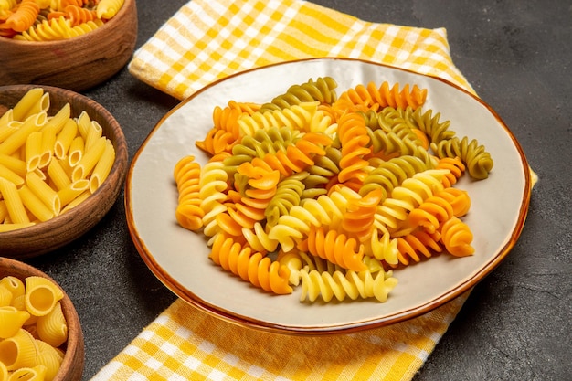 Vista frontale pasta italiana cruda diversa formata all'interno di piatti su scrivania grigia che cucina pasta italiana cruda