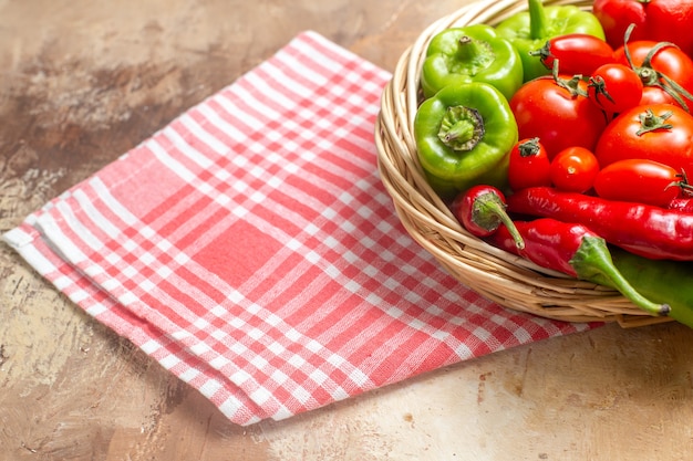 Vista frontale peperoni verdi e rossi peperoni pomodori in cesto di vimini asciugamano da cucina su ambra