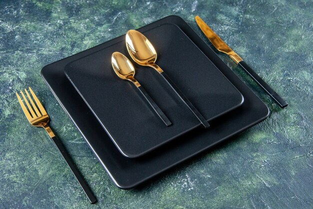 vista frontale piatti scuri con cucchiai d'oro, forchetta e coltello su sfondo blu scuro