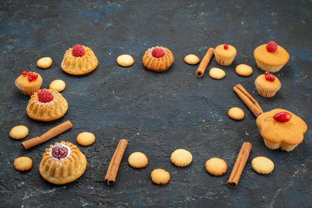 Vista frontale piccole torte squisite con crema di biscotti alla cannella sulla bacca di frutta dessert torta biscotto scrivania scura