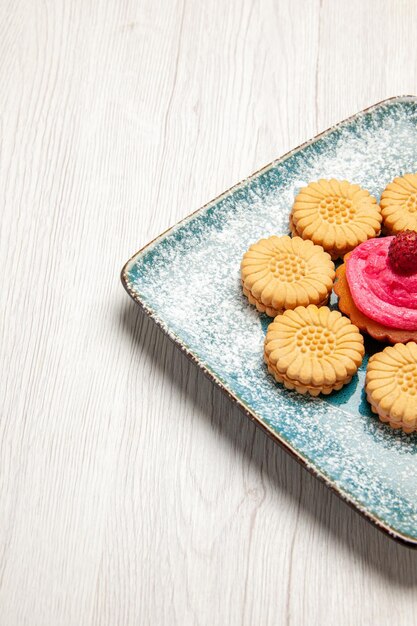 Vista frontale piccoli biscotti dolci con torta di frutta all'interno del piatto sulla scrivania bianca biscotto dolce biscotto zucchero torta