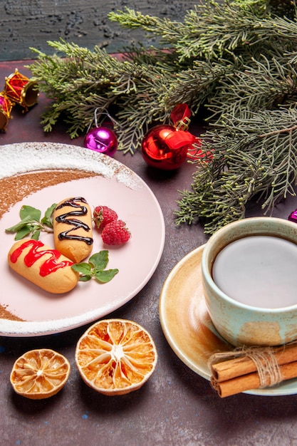 Vista frontale piccoli biscotti dolci con una tazza di tè su uno spazio buio