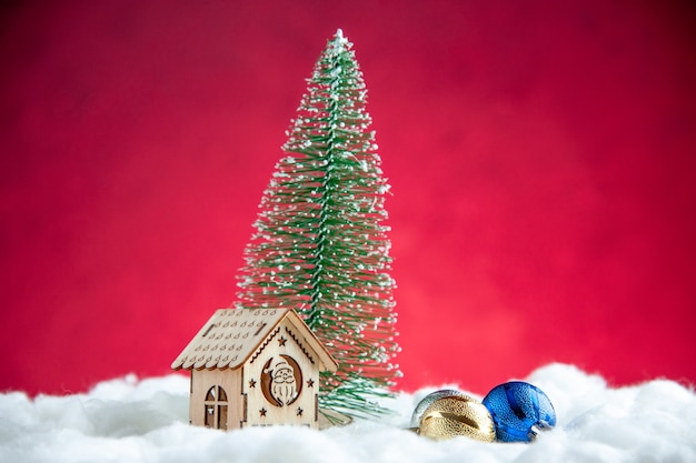 Vista frontale piccolo albero di natale piccola casa di legno su superficie rossa