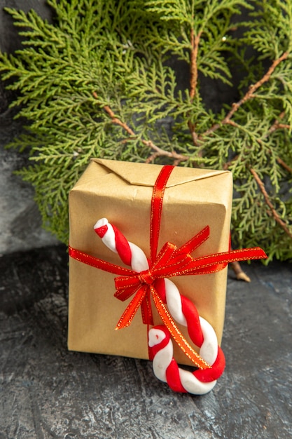 Vista frontale piccolo regalo legato con nastro rosso Natale caramelle rami di pino su sfondo grigio
