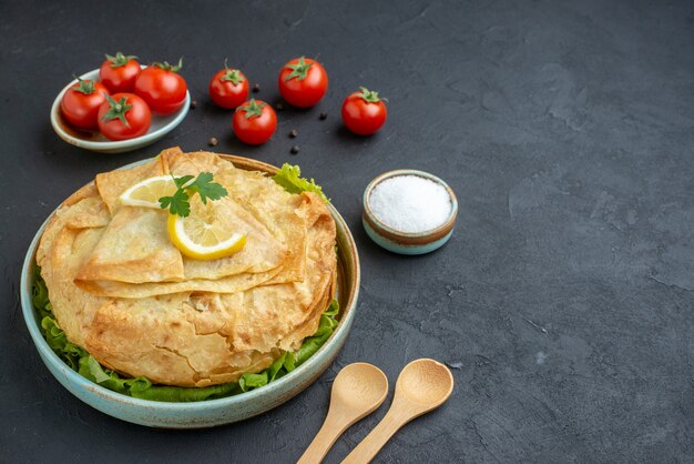 Vista frontale pita cotta all'interno del piatto con verdure, limone e pomodori sulla superficie scura