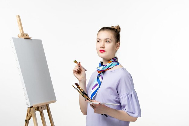 Vista frontale pittrice che si prepara a disegnare su una foto di arte della parete bianca disegnare una matita da cavalletto dell'artista di vernice