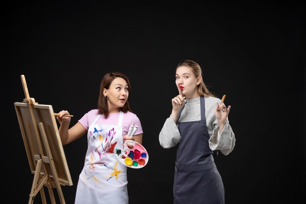 vista frontale pittrice disegno su cavalletto con altra donna su parete nera mostra foto colore arte immagine artista lavoro di pittura