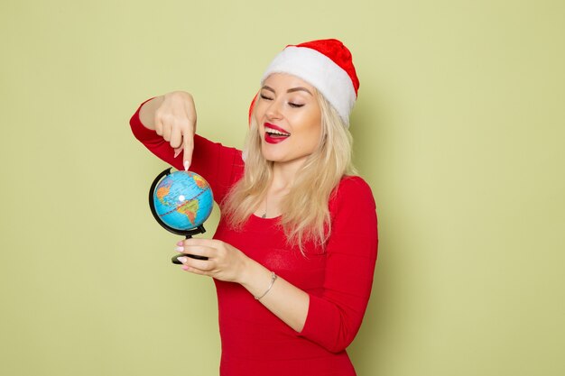 Vista frontale piuttosto femmina che tiene piccolo globo terrestre sul colore di emozione del nuovo anno della neve di Natale di festa della parete verde