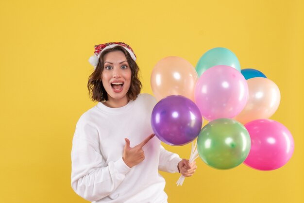 Vista frontale piuttosto femminile che tiene palloncini colorati su giallo