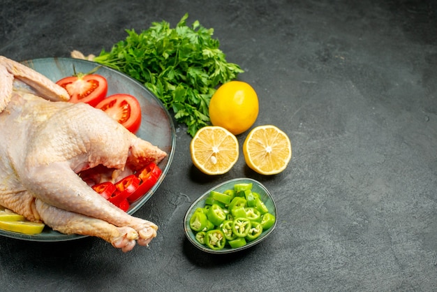 Vista frontale pollo fresco crudo all'interno del piatto con limone verde e verdure su sfondo scuro colore alimentare carne pollo animale