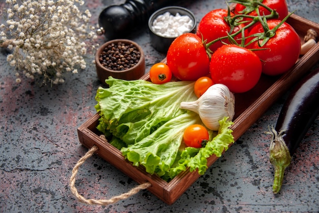 vista frontale pomodori rossi freschi con aglio e insalata verde all'interno della tavola di legno su sfondo blu