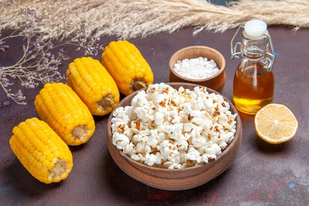 Vista frontale popcorn fresco con semi gialli crudi e olio su pianta di film di mais popcorn snack superficie scura dark