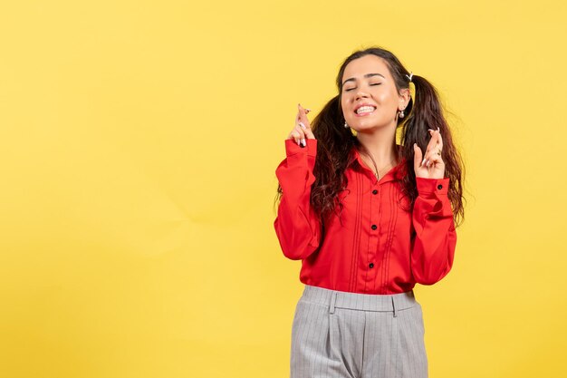 Vista frontale ragazza in camicetta rossa con capelli carini e faccia felice su sfondo giallo innocenza bambino ragazza gioventù colore bambino