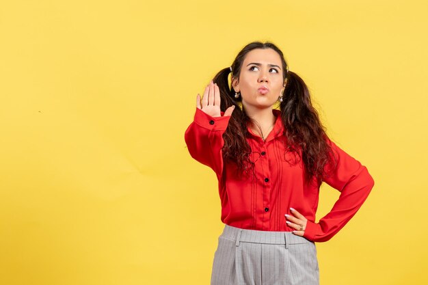 Vista frontale ragazza in camicetta rossa con capelli carini e faccia sognante su sfondo giallo innocenza bambino ragazza gioventù colore bambino