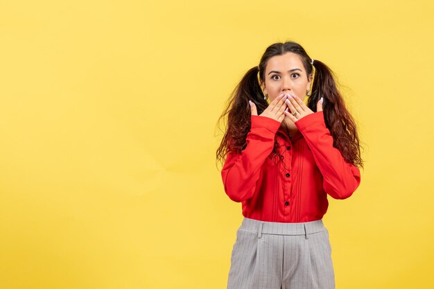 Vista frontale ragazza in camicetta rossa con capelli carini e viso scioccato su sfondo giallo bambino ragazzo ragazza gioventù colore innocenza