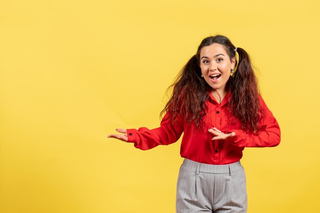 Vista frontale ragazza in camicetta rossa con capelli carini in posa su sfondo giallo bambino ragazza gioventù innocenza colore bambino