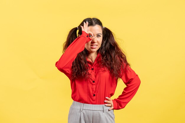 Vista frontale ragazza in camicetta rossa con capelli carini in posa su sfondo giallo bambino ragazza gioventù innocenza colore bambino