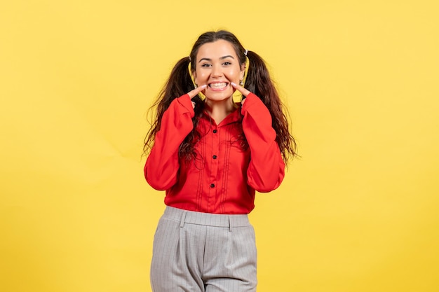 Vista frontale ragazza in camicetta rossa con sorriso su sfondo giallo sentimento femminile bambino bambina ragazza emozione giovanile