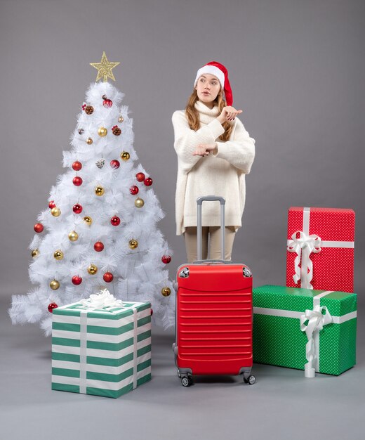 Vista frontale ragazza sorpresa con la valigia rossa in piedi vicino all'albero di Natale