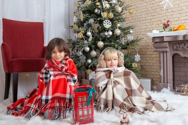 Vista frontale ragazzini carini seduti intorno all'albero di Natale e regali nella loro casa