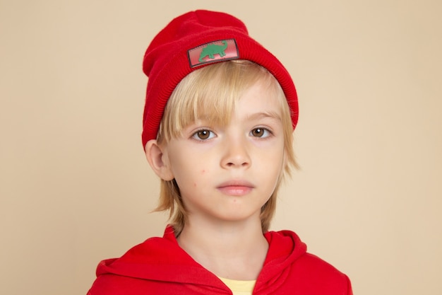 Vista frontale ragazzino carino in camicia rossa e berretto sul muro bianco