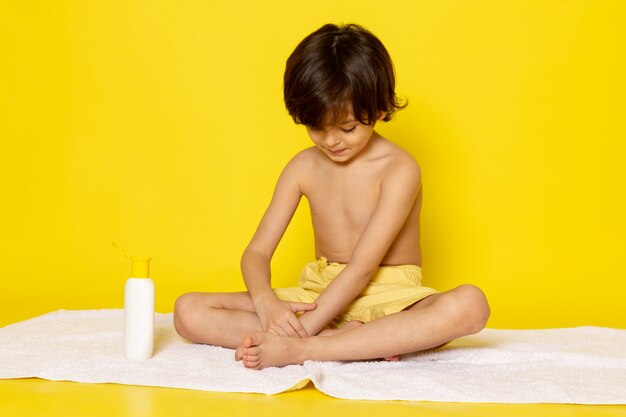 vista frontale ragazzo carino sorridente seduto sul telo bianco sul giallo