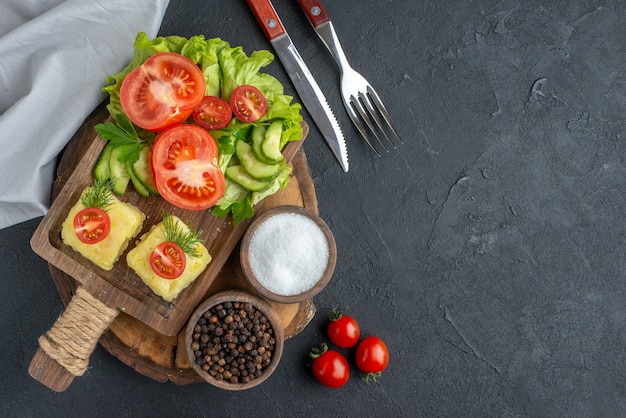 Vista frontale ravvicinata del formaggio di verdure fresche tritate e intere su tagliere e spezie sul lato destro su superficie nera