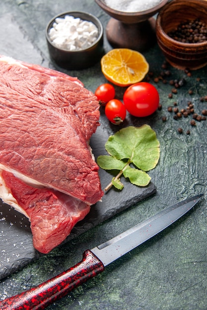 Vista frontale ravvicinata di carne rossa cruda fresca su vassoio nero pepe sale limone coltello a martello in legno su sfondo di colore scuro