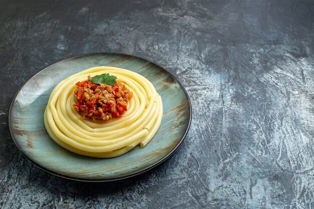 Vista frontale ravvicinata di un delizioso pasto di pasta su un piatto blu servito con pomodoro e carne per cena sul lato destro