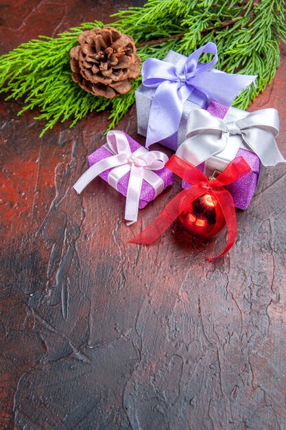 Vista frontale regali di natale ramo di albero con cono albero di natale giocattolo su rosso scuro
