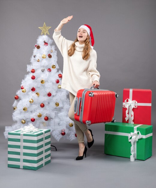 Vista frontale salutando la ragazza con il cappello della santa che tiene la sua borsa da viaggio vicino all'albero di Natale bianco