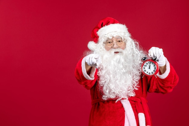 Vista frontale santa claus che tiene l'orologio su rosso natale emozione vacanza capodanno