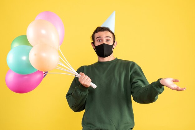 Vista frontale si chiedeva il giovane con cappello da festa e palloncini colorati in piedi sul giallo