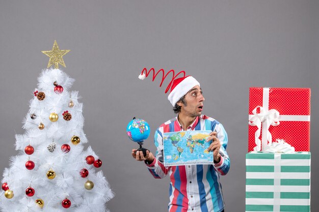 Vista frontale si chiedeva l'uomo con il cappello della santa a spirale della molla che esamina i regali che tengono la mappa e il globo del mondo