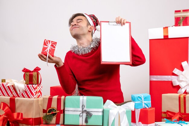 Vista frontale soddisfatto giovane azienda regalo e appunti seduti intorno a regali di Natale