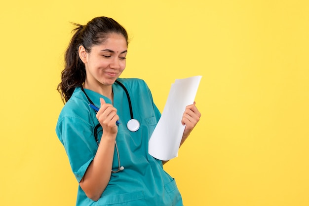 Vista frontale soddisfatto medico femminile in possesso di documenti su sfondo giallo