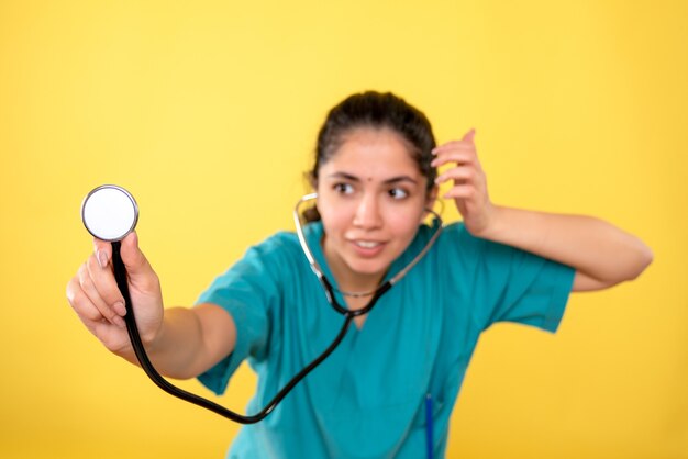 Vista frontale sorrise medico donna in uniforme tenendo lo stetoscopio su sfondo giallo isolato