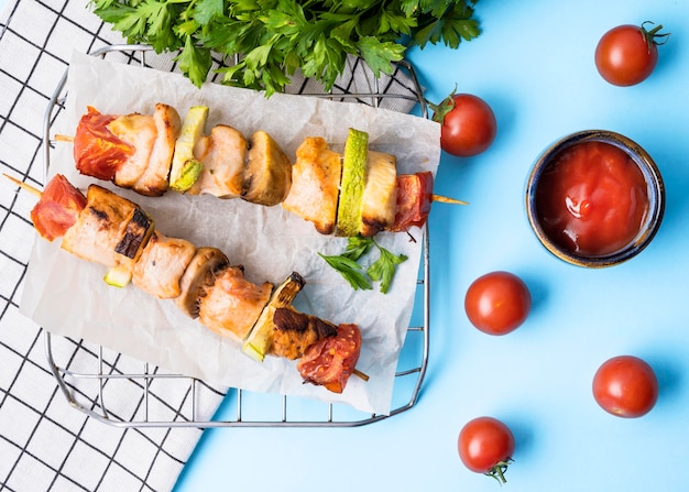 Vista frontale spiedini di pollo su carta pergamena con pomodorini e salsa