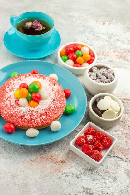 Vista frontale squisita torta rosa con caramelle colorate e tazza di tè su sfondo bianco torta da dessert color arcobaleno caramelle