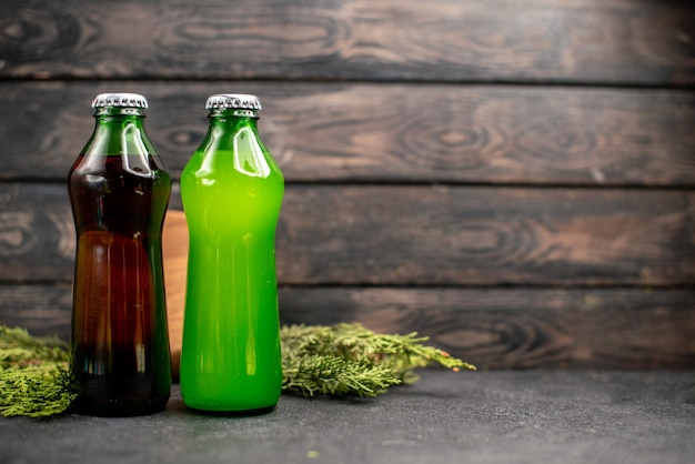Vista frontale succhi neri e verdi in bottiglie rami di pino su tavola di legno