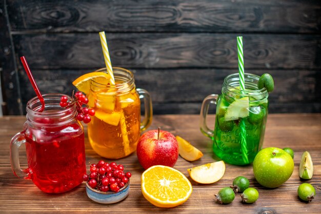Vista frontale succo fruttato fresco arancia feijoa e bevande al mirtillo rosso all'interno di lattine sulla scrivania marrone bere foto cocktail colore frutti