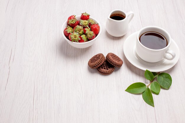 Vista frontale tazza di tè con biscotti al cioccolato e fragole su scrivania bianca zucchero tè biscotti dolce biscotto