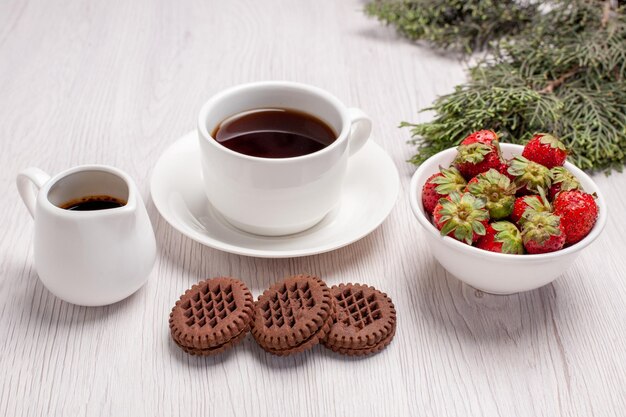 Vista frontale tazza di tè con biscotti e fragole su scrivania bianca zucchero tè biscotti biscotto dolce