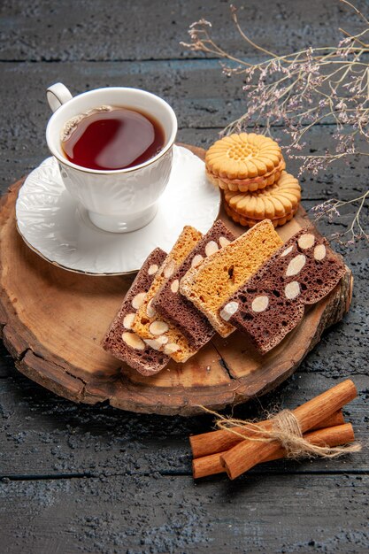 Vista frontale tazza di tè con biscotti e torte sulla scrivania scura