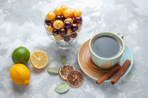 Vista frontale tazza di tè con cannella, limone e ciliegie sulla scrivania bianca bere tè color cannella limone