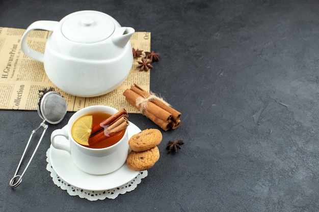 Vista frontale tazza di tè con cannella marrone e biscotti su sfondo scuro pasto cerimonia colazione pranzo tavolo cibo colore limone