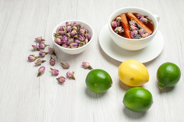 Vista frontale tazza di tè con fiori e limoni su scrivania bianca tè frutta agrumi colore