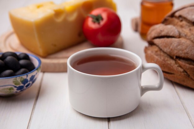 Vista frontale tazza di tè con formaggio olive pomodoro su un supporto e una pagnotta di pane nero su sfondo bianco