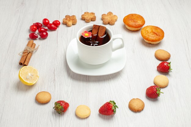 Vista frontale tazza di tè con frutta e biscotti sul biscotto dessert tè bianco scrivania