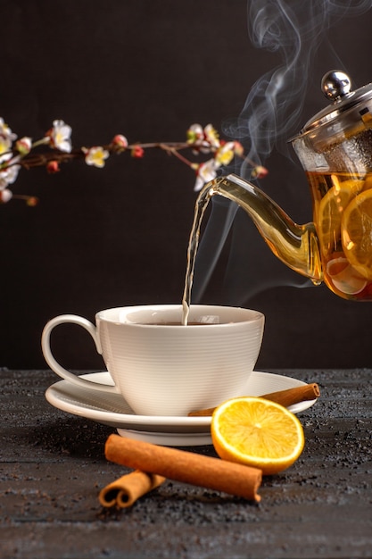 Vista frontale tazza di tè con limone cannella e bollitore sulla scrivania grigia